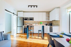 A modern kitchen with white cabinets, stainless steel appliances, and a wooden dining table with bar stools. - Double Suite @ Guest Inn 2 Boutique House (campo pequeno)