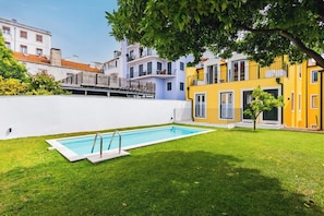 A swimming pool with a white deck, surrounded by a well-maintained lawn, and adjacent to a yellow building with balconies. - Lapa Getaway Studio with Swimming Pool (Lisbon)