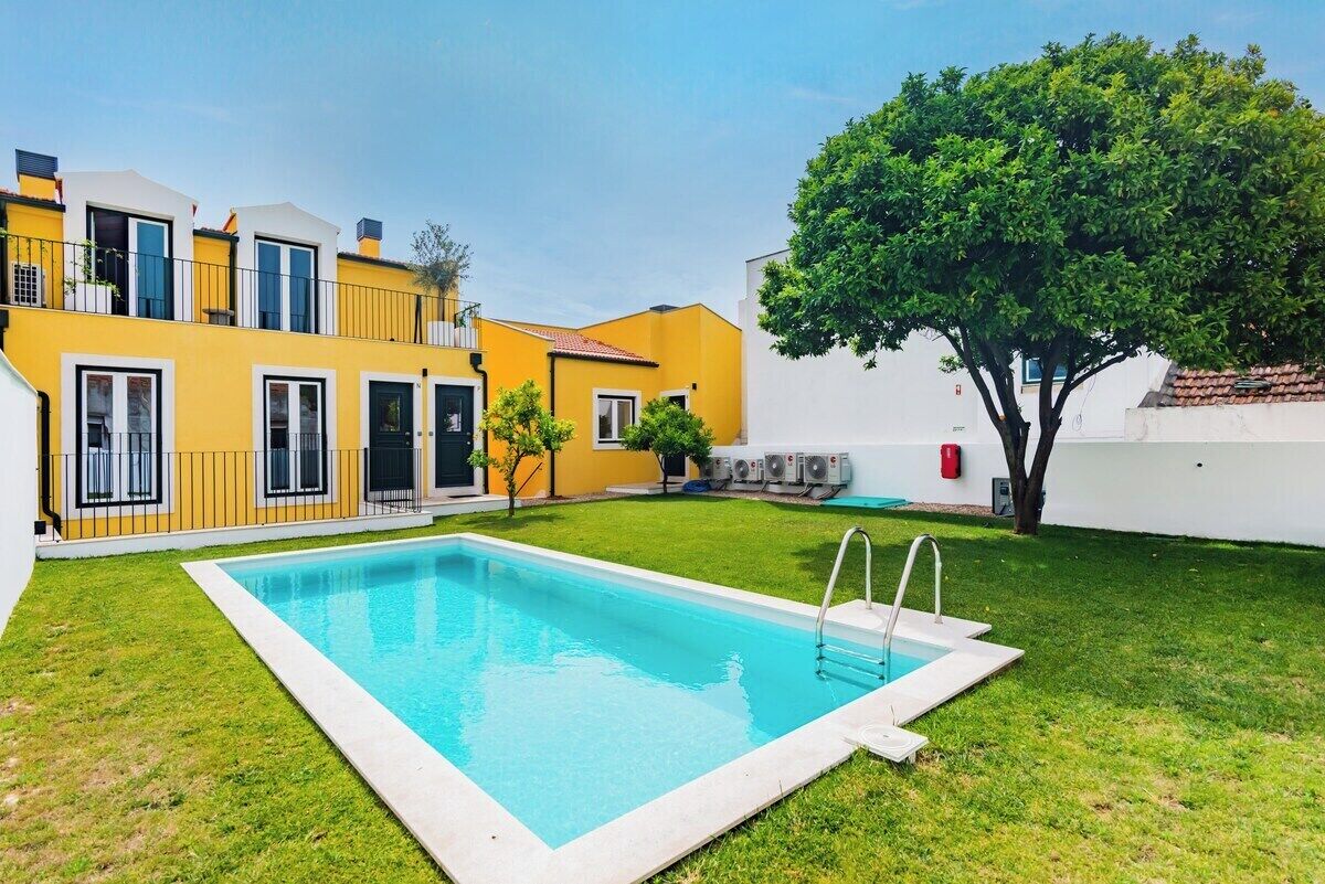 A residential building with a swimming pool, a tree, and a white wall.
