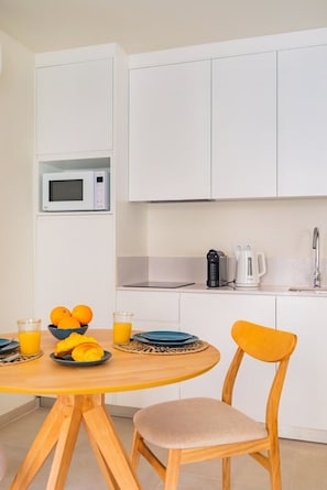 A compact kitchen with white cabinets, a microwave, a coffee maker, and a sink. There's a wooden table with plates and oranges. - Lapa Getaway Studio with Swimming Pool (Lisbon)