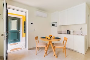 A compact kitchen with white cabinets, a microwave, and a coffee maker. There is a dining table with chairs and a fruit bowl. - Lapa Getaway Studio with Swimming Pool (Lisbon)