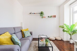 A modern living room with a grey sofa, a glass coffee table, and a white wall with shelves. - Saldanha Charm Hideaway (Lisbon)