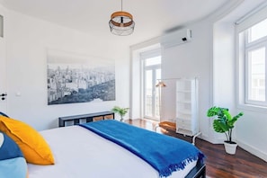 A modern bedroom with a bed, a cityscape painting, a hanging light fixture, and a potted plant. - Saldanha Charm Hideaway (Lisbon)