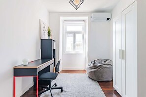 Habitación pequeña con escritorio, silla, sillón de peluche y ventana.