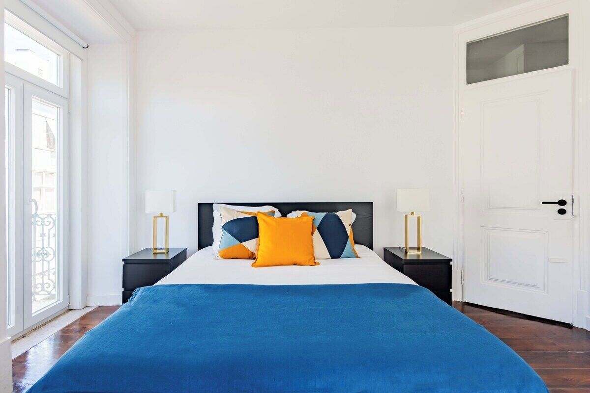 Une chambre à coucher avec un lit, deux tables de chevet, une fenêtre et une porte.