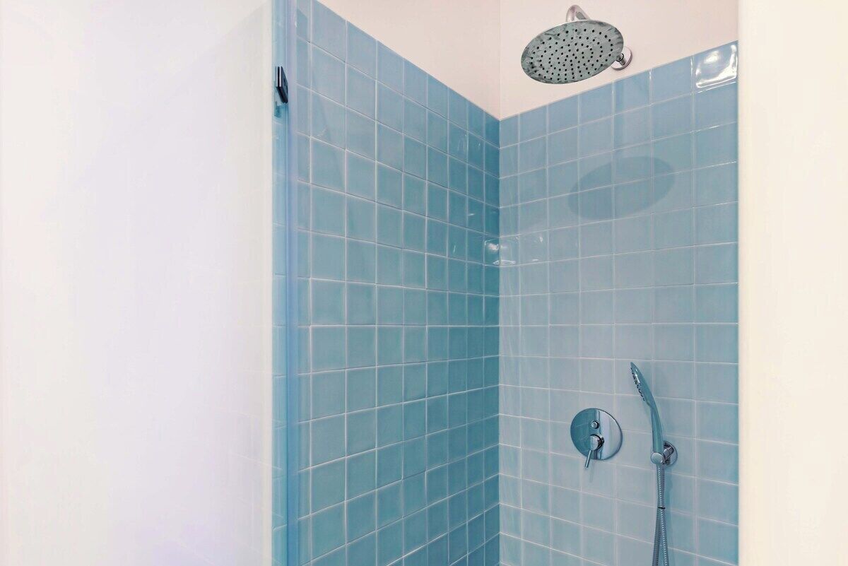 Ducha en esquina con azulejos azules y un cabezal de ducha manual.