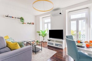 A living room with a sofa, coffee table, TV, and dining area with a balcony view. - Saldanha Charm Hideaway (Lisbon)