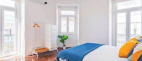 A bedroom with a bed, a bedside table, a floor lamp, a window, and a plant.