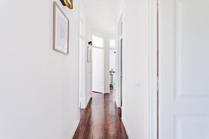 Un pasillo con paredes blancas, suelo de madera y cuadros enmarcados.