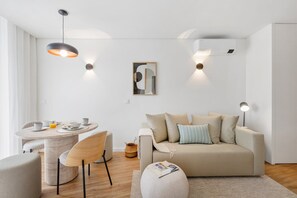 A modern living room with a round dining table, a sofa, and a coffee table. - Sage 1BR | Balconies, AC & Parking (Porto)