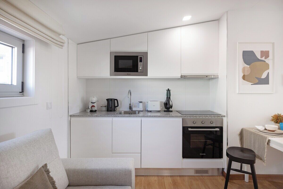 Una cocina compacta con gabinetes blancos, microondas integrado, estufa y lavamanos.