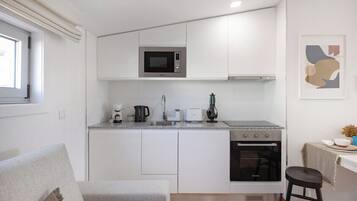 Una cocina compacta con gabinetes blancos, microondas integrado, estufa y lavamanos.