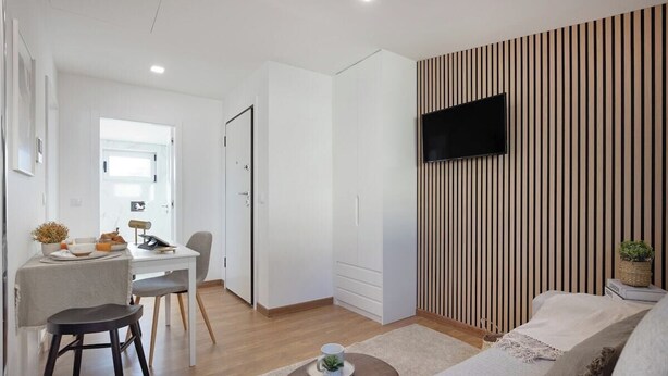 A modern living room with a sofa, a coffee table, a TV mounted on a striped wall, and a dining area with a table and chairs. - Matosinhos Seaside Comfy Flat (Matosinhos)