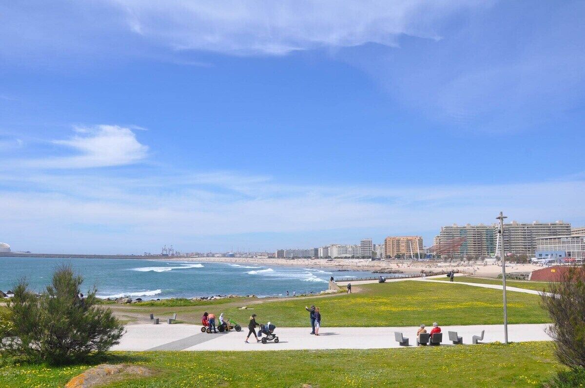 A coastal park with a walking path, grassy areas, and a view of the ocean and buildings in the distance.