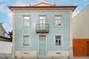 Een gebouw met een betegelde gevel, een centrale ingang en een balkon met een metalen hekwerk.