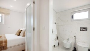 A bedroom with a bed, a bedside table, and a window. The bathroom includes a toilet, a bidet, a sink, and a mirror. - Matosinhos Seaside Comfy Flat (Matosinhos)