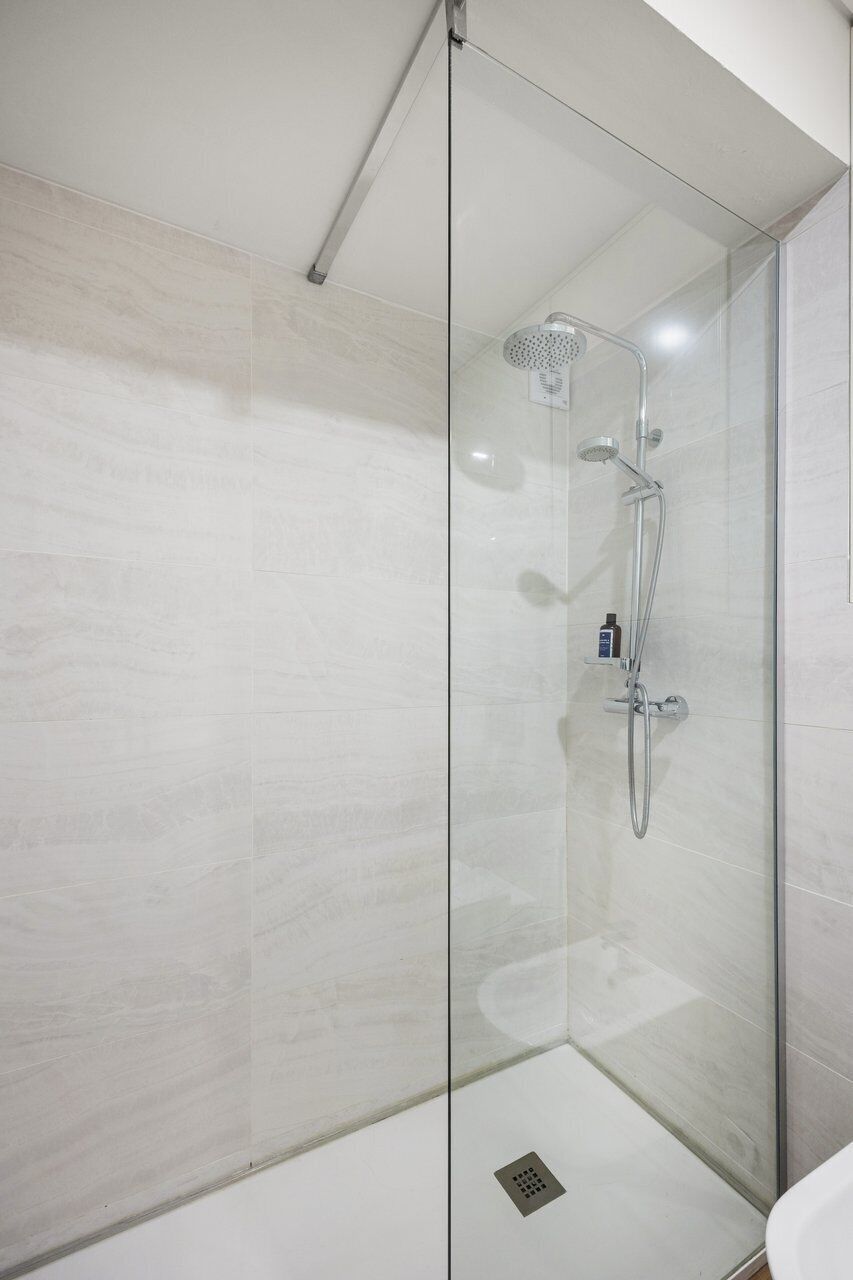 A glass-enclosed shower with a handheld showerhead and a wall-mounted faucet.