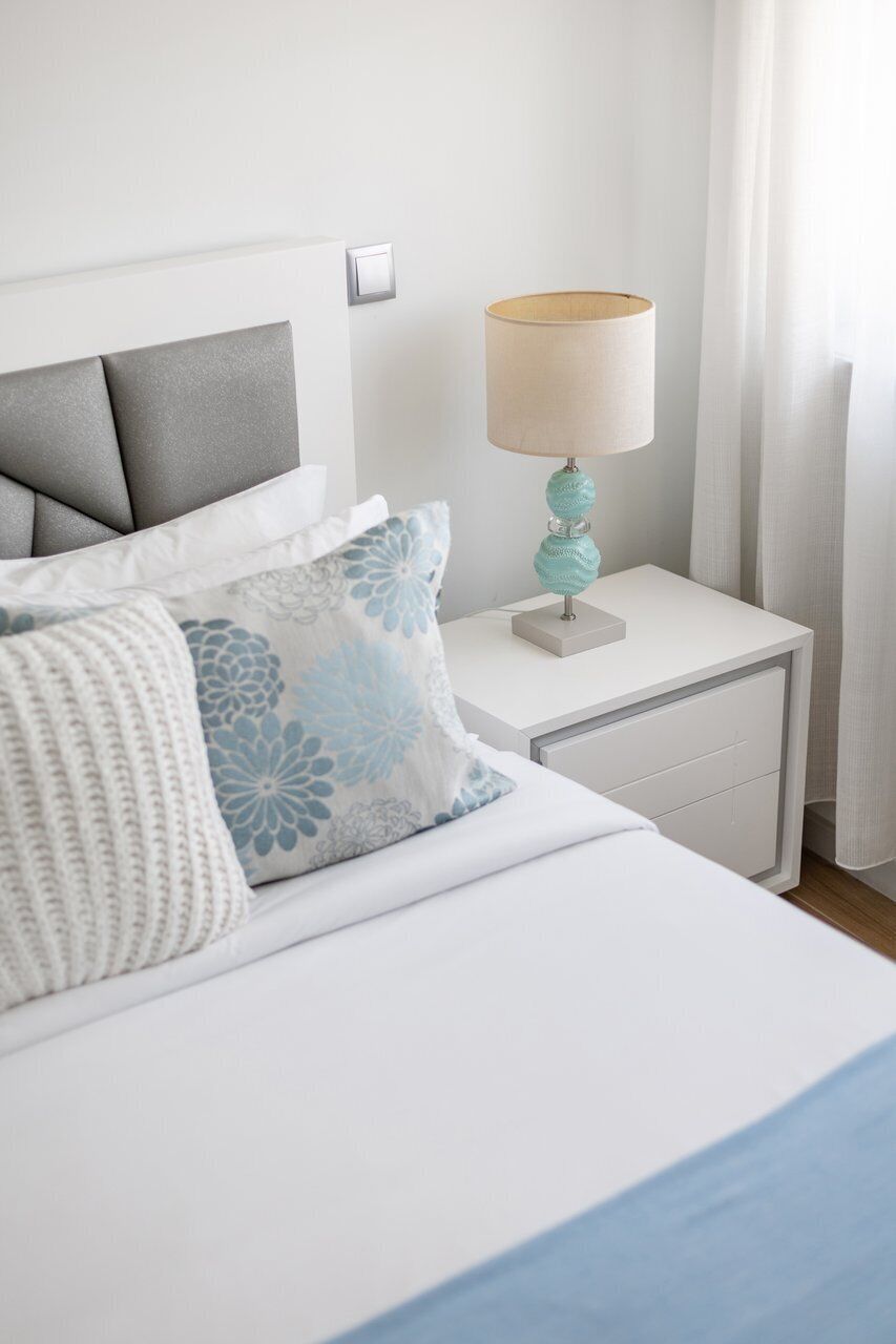 A neatly made bed with a headboard, a bedside lamp, and a nightstand with a drawer.