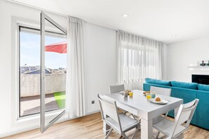 Ein modernes Wohnzimmer mit Essbereich, einem blauen Sofa und einem Balkon mit einem roten Sonnenschirm.