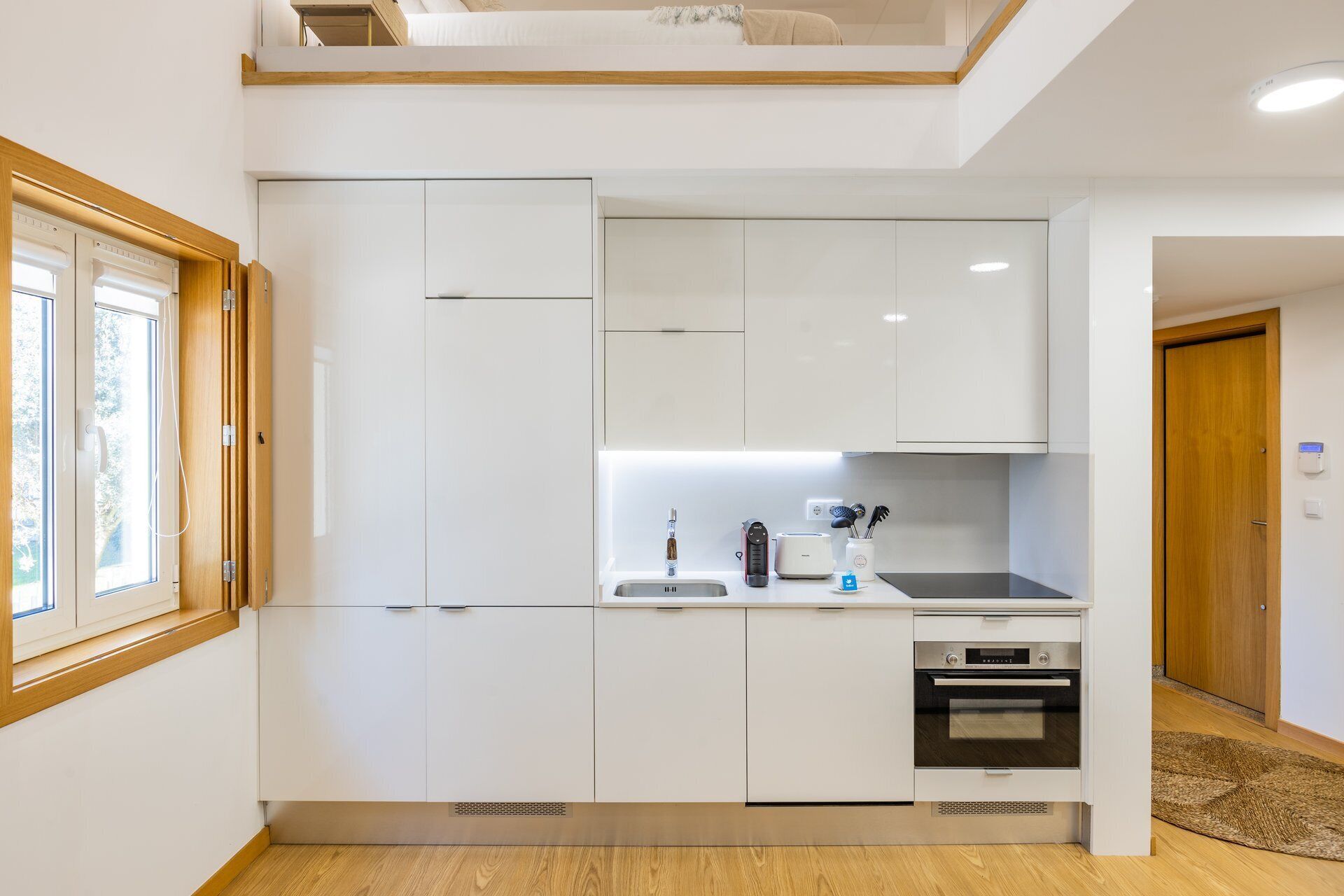 A modern kitchen with white cabinets, a built-in oven, and a window.