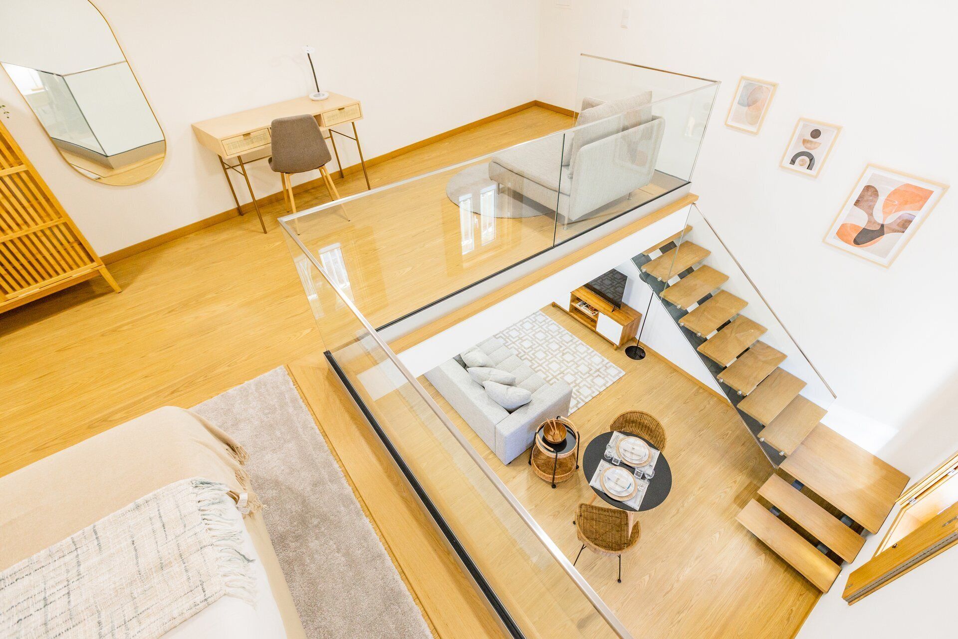 Un intérieur moderne avec un pont de verre reliant deux niveaux, un canapé, une table avec des chaises et un escalier.