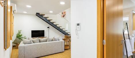 Una sala de estar moderna con un sofá, un televisor, una escalera y piso de madera.