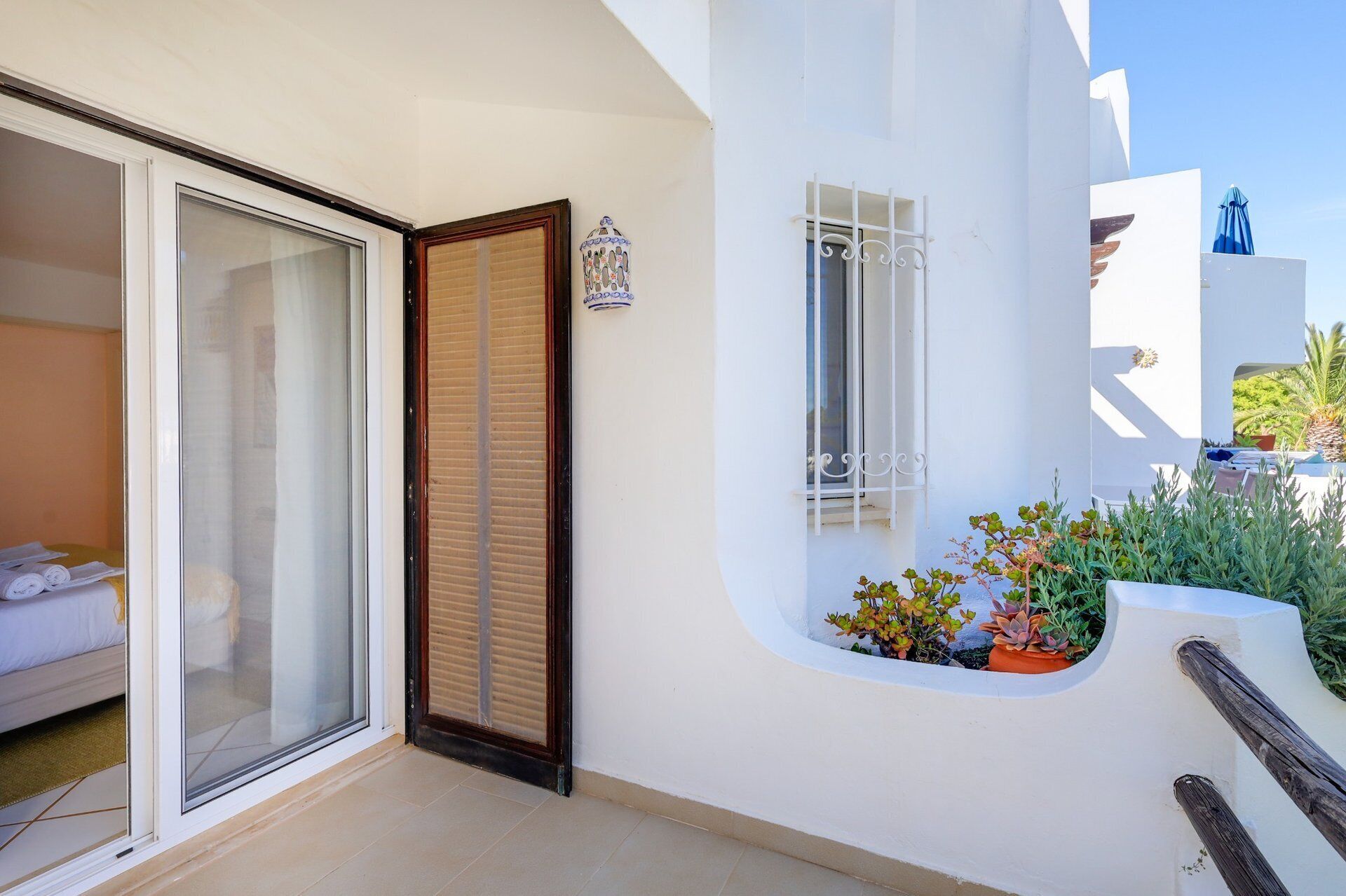 Un bâtiment moderne doté d’une porte en verre, d’un petit balcon agrémenté de plantes et d’une façade blanche.
