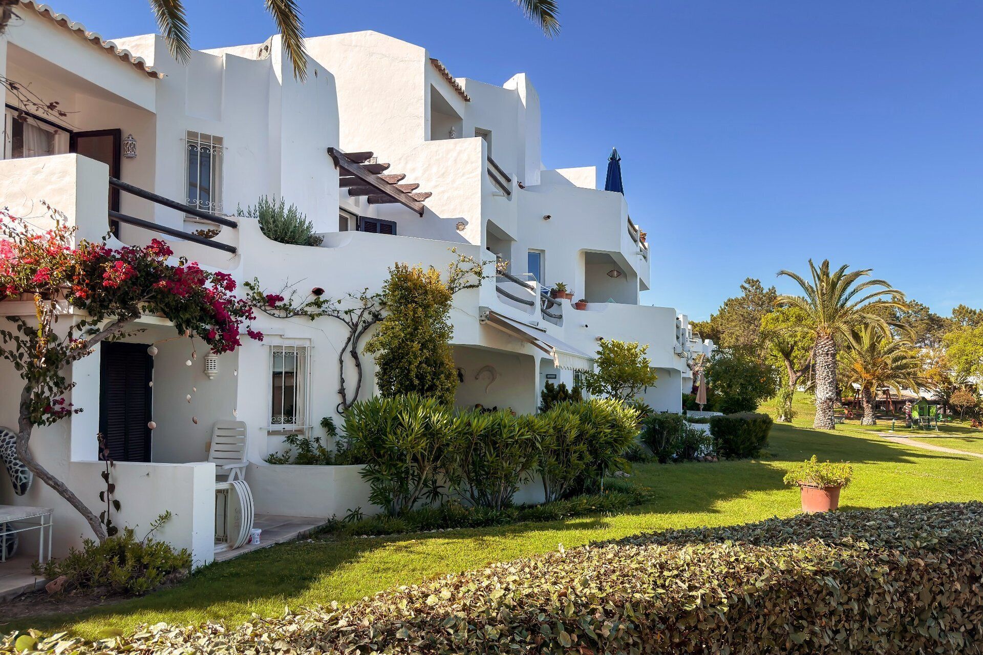 A white building with balconies, a garden, and a clear blue sky.