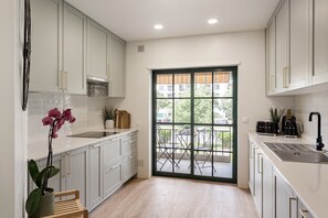 A modern kitchen with white cabinets, a black countertop, a sink, and a window with a view of the outside. - Carcavelos Terrace & Beach Apartment (Carcavelos)