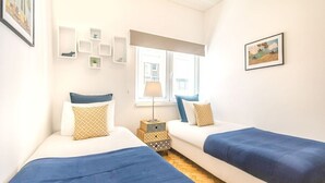 Ein Schlafzimmer mit zwei Betten, einem Fenster, einer Lampe und Wanddekorationen.