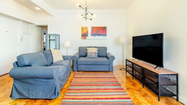 Ein Wohnzimmer mit zwei Sofas, einem Fernseher und einem farbenfrohen Streifen Teppich.