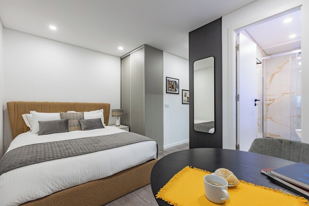 A modern hotel room with a large bed, a desk with a laptop, a chair, and a bathroom with a marble shower.