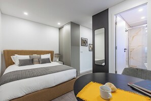 A modern hotel room with a large bed, a desk with a laptop, a chair, and a bathroom with a marble shower. - Cantar o Fado @ Boavista Executive Studios (Porto)