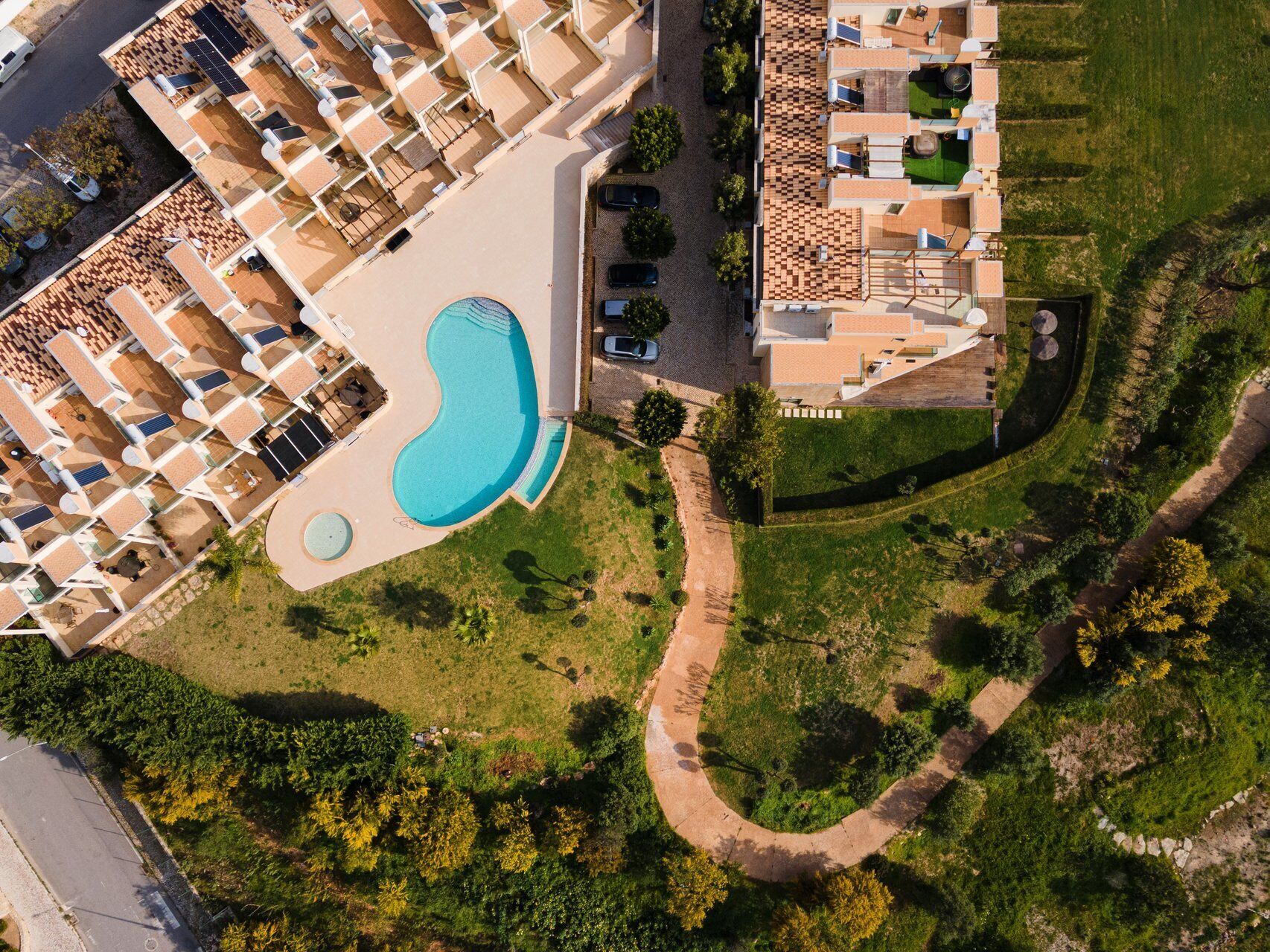 Luchtbeeld van een hotel met een zwembad, meerdere balkons en een aangelegde tuin.