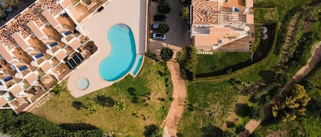 An aerial view of a hotel with a swimming pool, multiple balconies, and a landscaped garden.