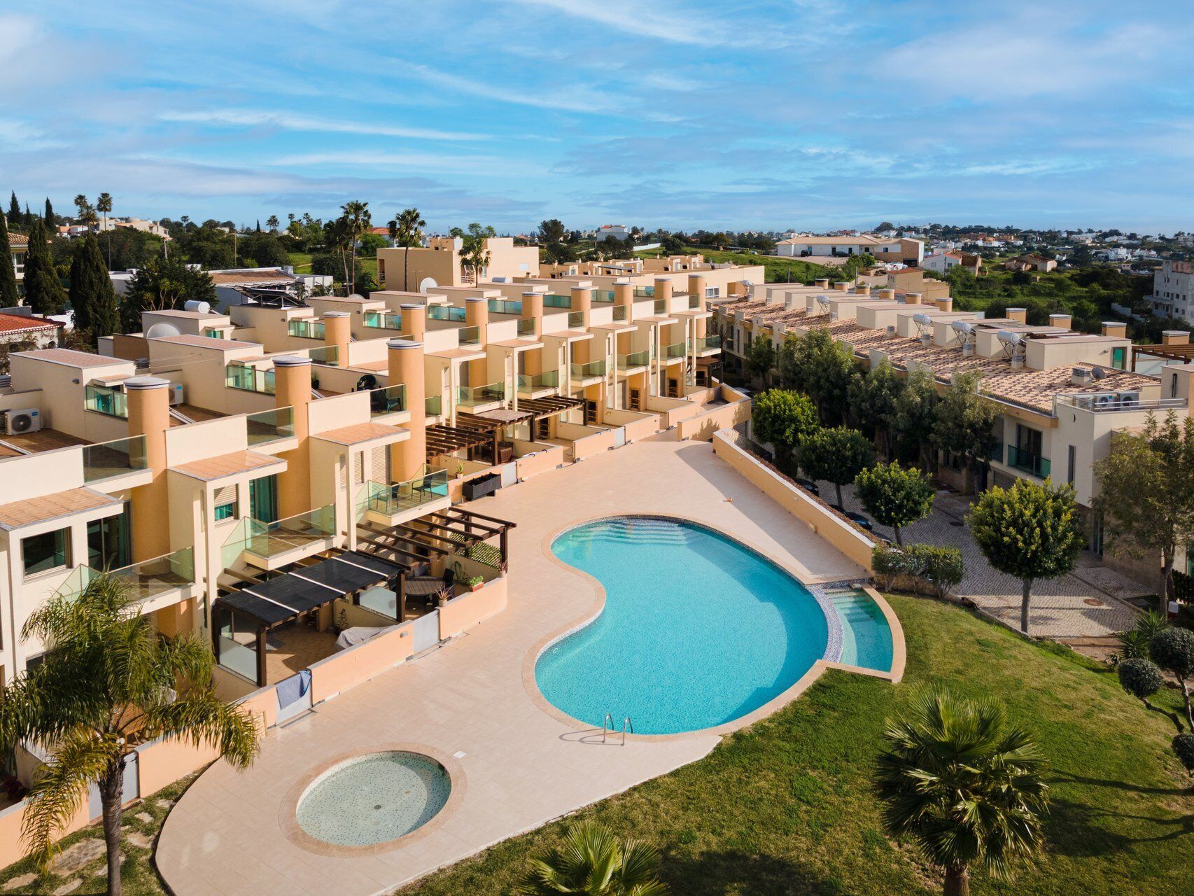 A hotel with multiple balconies, a central swimming pool, and surrounding greenery.