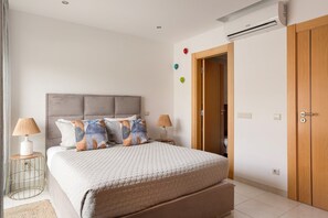 A bedroom with a bed, bedside lamps, a wooden door, and an air conditioning unit. - Albufeira Poolside Family Vila (Albufeira)