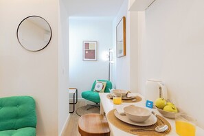 A compact living space with a dining area, a green chair, a round mirror, and a kitchenette. - Studio Dash | 111 Collection (Porto)