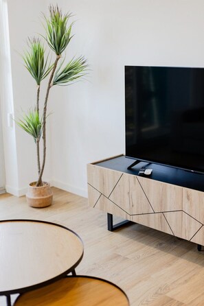 Ein modernes Wohnzimmer mit Flachbildfernseher auf einem Holzschrank, einem Blumentopf und einem runden Esstisch.
