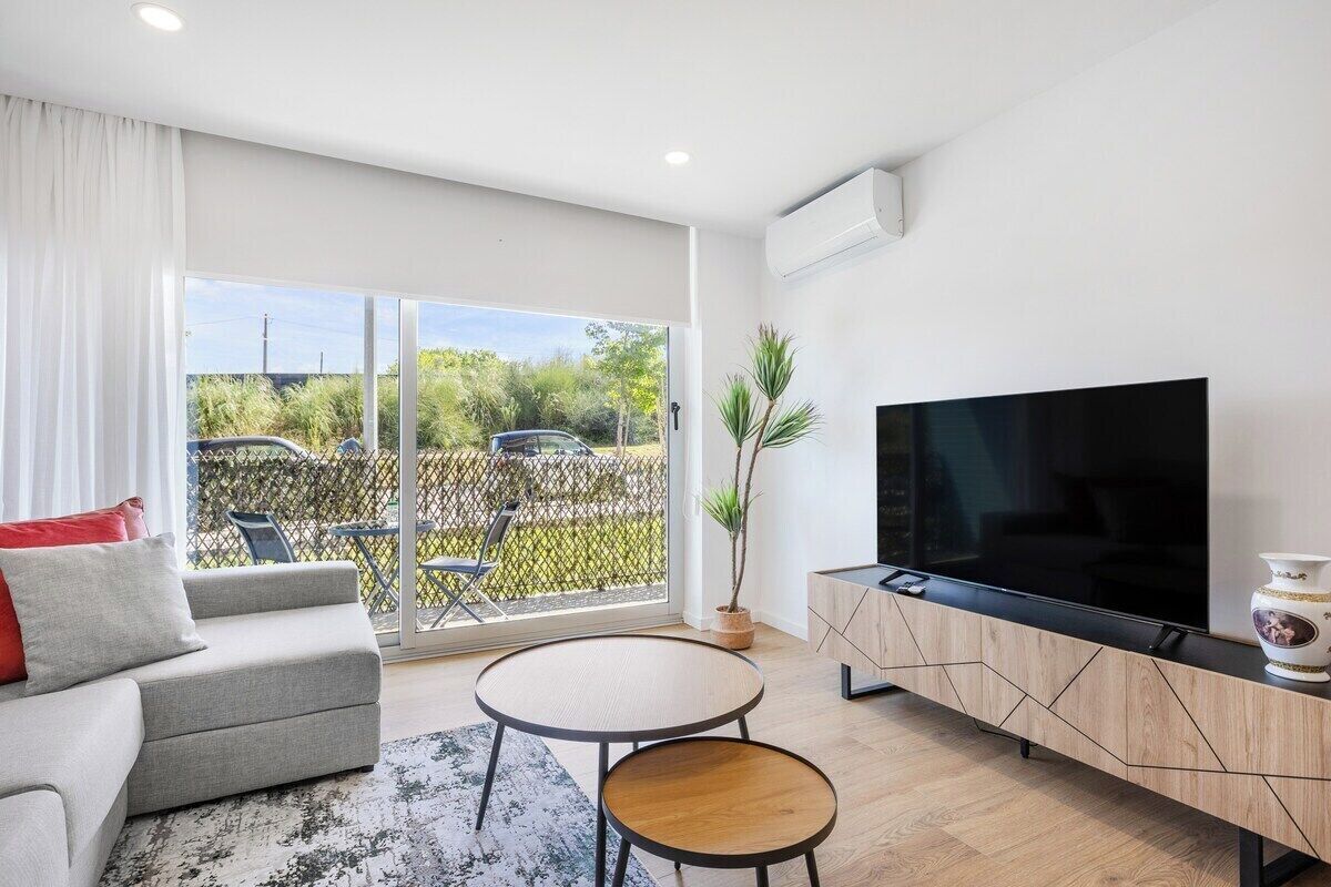 En moderne stue med sofa, fjernsyn, lille bord og skydedør til et udendørs område.