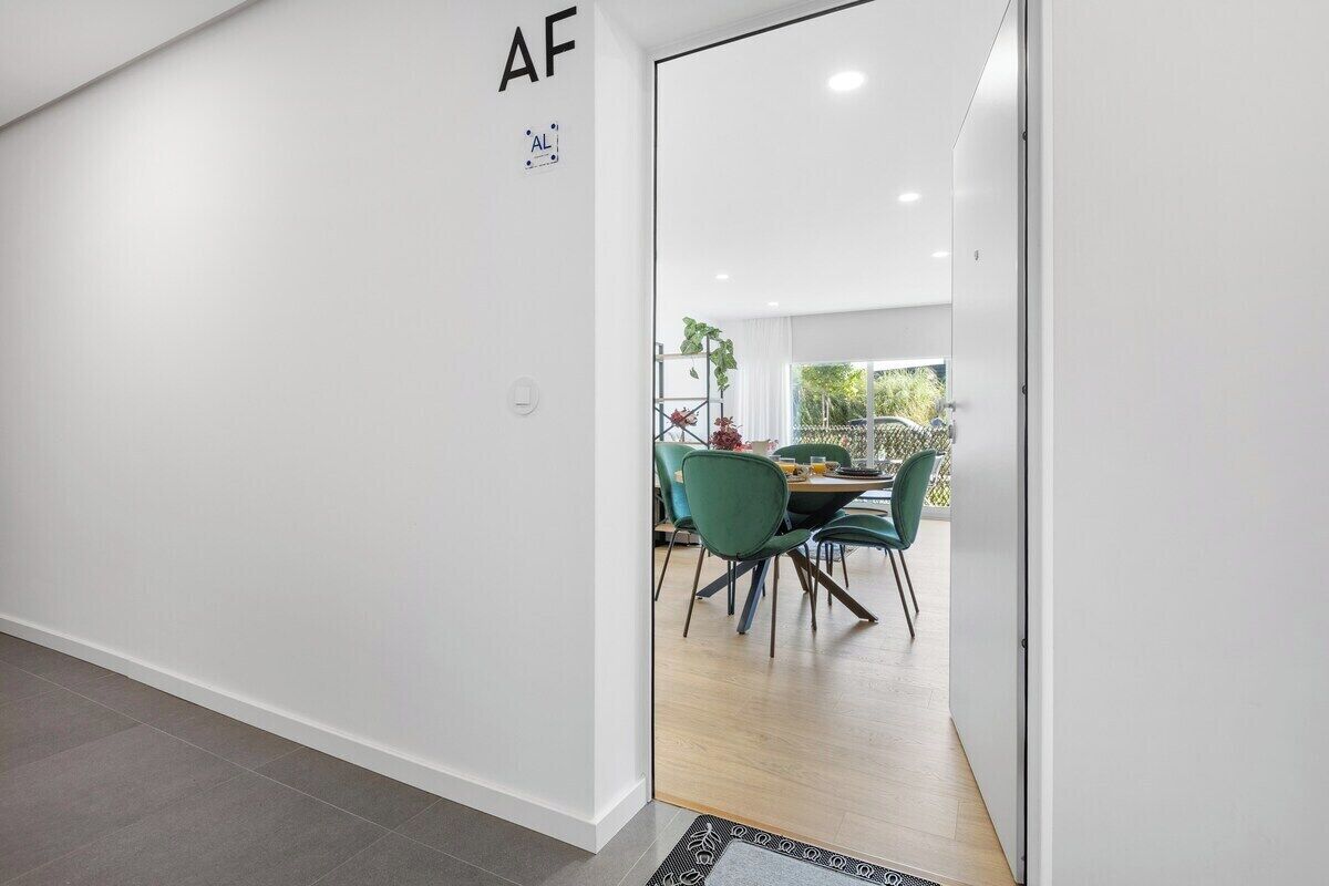 Un interior moderno con una zona de comedor que incluye una mesa y sillas, una puerta visible con un letrero, y vistas a través de la ventana.