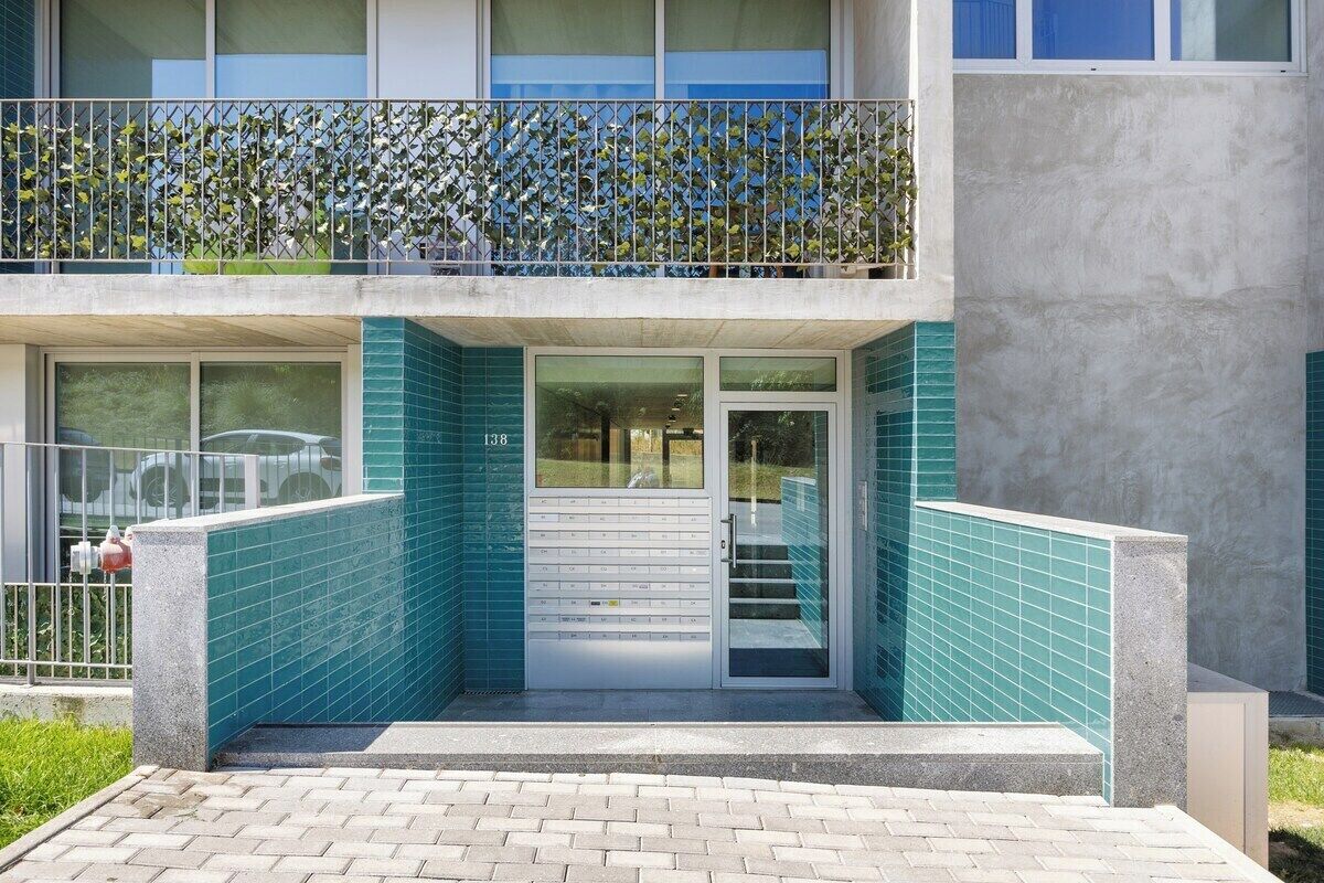 A building with a modern design, featuring a glass entrance, a balcony with a metal railing, and a staircase leading to the entrance.