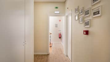 Un pasillo con piso de madera, paredes blancas y cuadros enmarcados a la derecha. Se observa un extintor y un cartel en la pared.