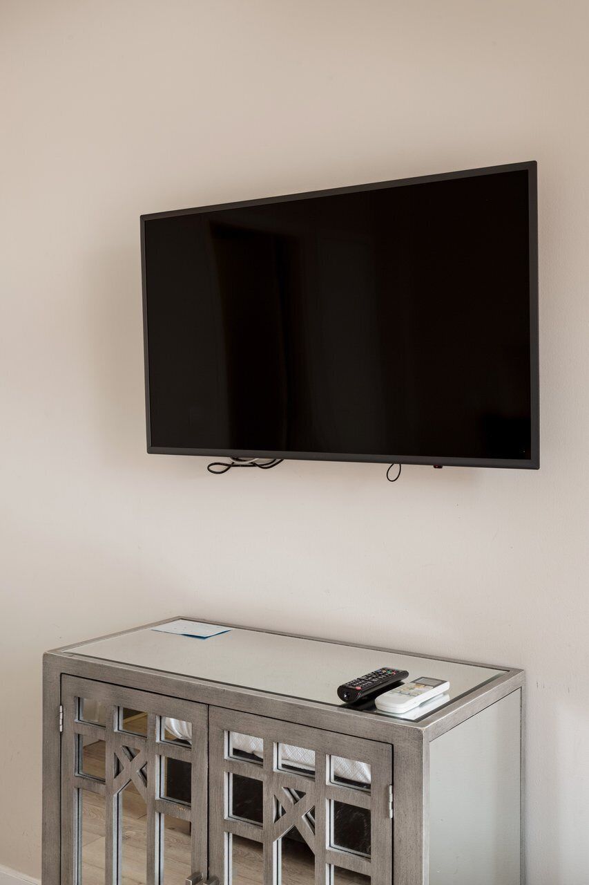 Ein Flachbildfernseher ist an einer Wand über einem grauen Konsolentisch montiert, zusammen mit einer Fernbedienung und einem Buch.