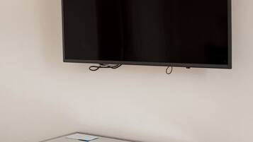 Ein Flachbildfernseher ist an einer Wand über einem grauen Konsolentisch montiert, zusammen mit einer Fernbedienung und einem Buch.