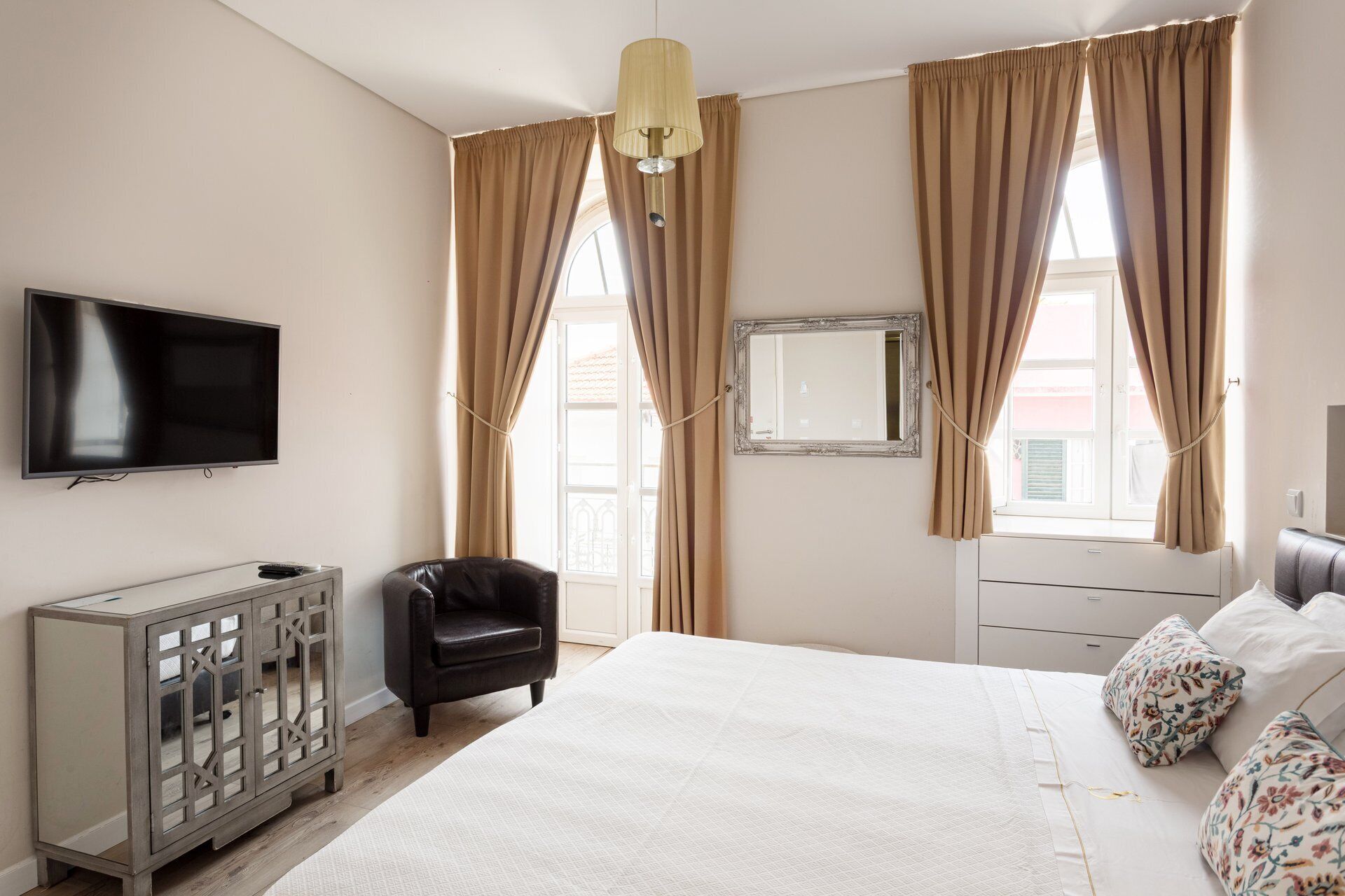 A bedroom with a bed, a television, a cabinet, a chair, and curtains.