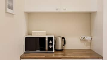 Una cucina con forno a microonde, bollitore ed una presa elettrica su un piano di lavoro in legno.