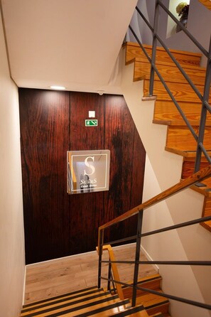 Una scala con gradini in legno e ringhiere metalliche conduce a un'oscura porta in legno con un'insegna che indica un'albergo.