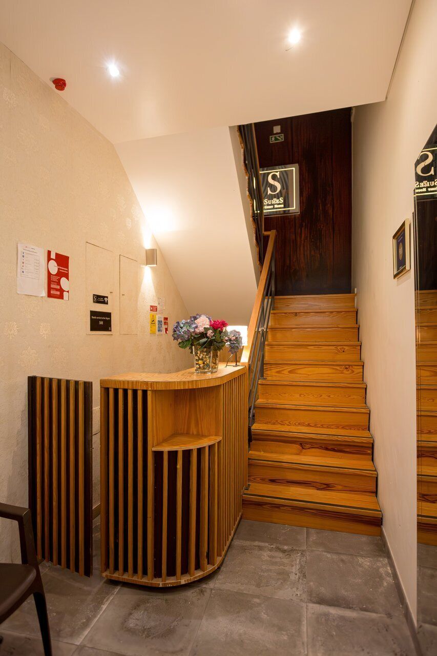 A reception desk with a wooden finish, a staircase with wooden steps, and a sign indicating the name of the establishment.