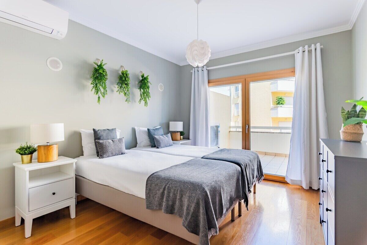 Une chambre à coucher comprenant un lit, des tables de chevet, une lampe, un ventilateur de plafond et une vue sur l’extérieur.
